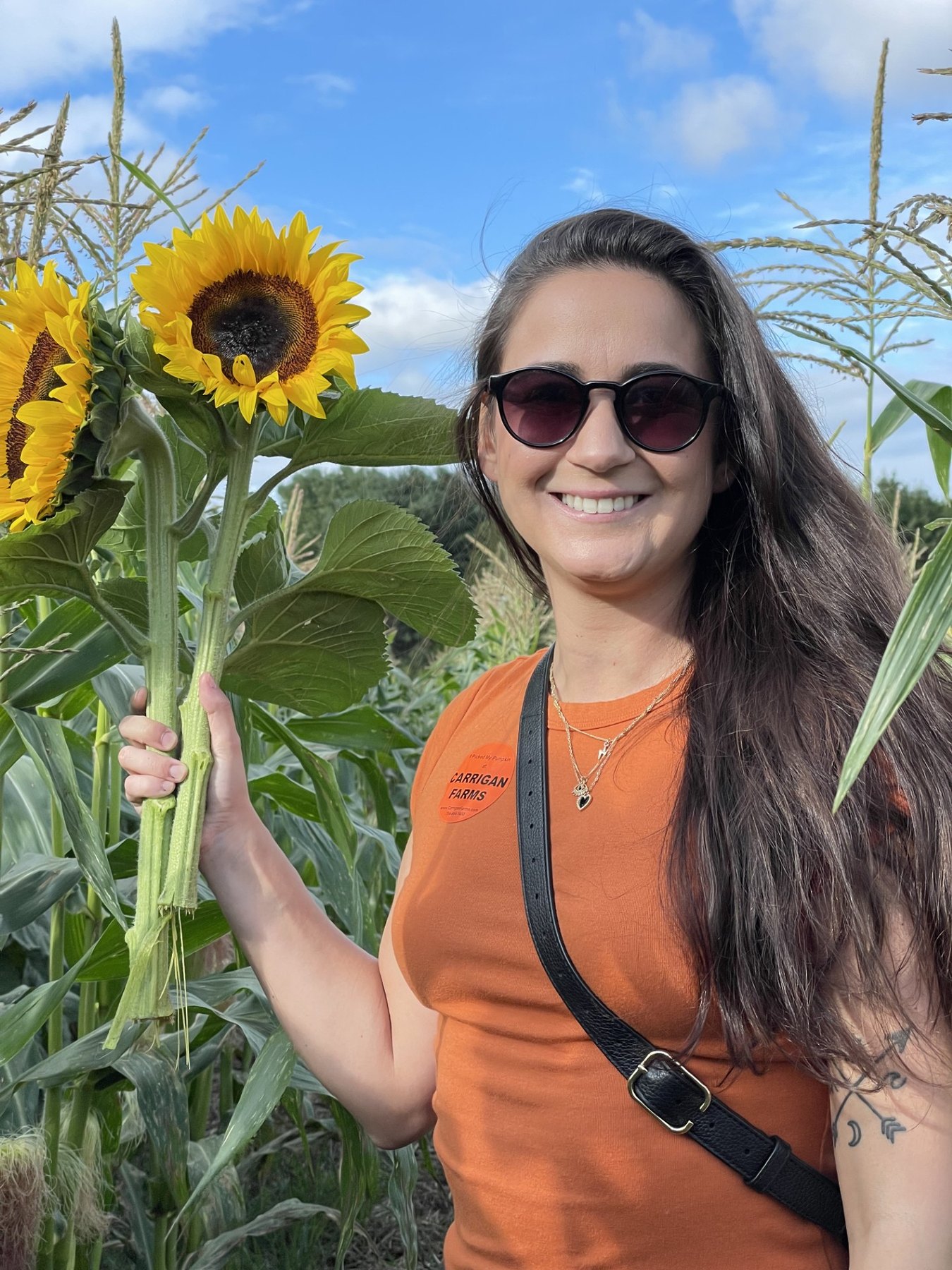 Shannon smiling in a sunflower field, holding a tall sunflower